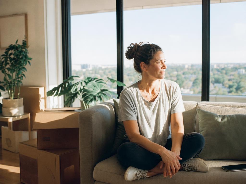 A woman sitting in a sunlit apartment with a few moving boxes nearby